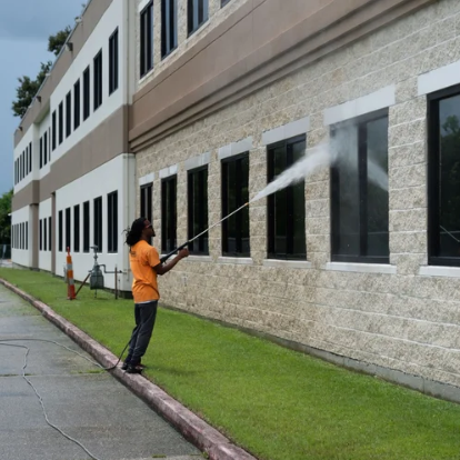 Person pressure-washing windows on the side of a building with a hose.