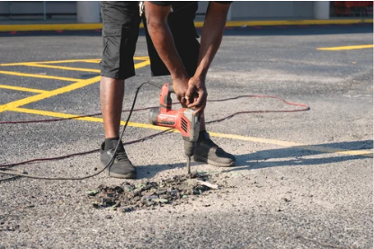 Worker using a jackhammer to break asphalt on a road repair site
