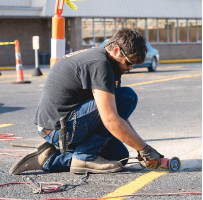 Worker kneeling and cutting pavement with an angle grinder in a parking lot