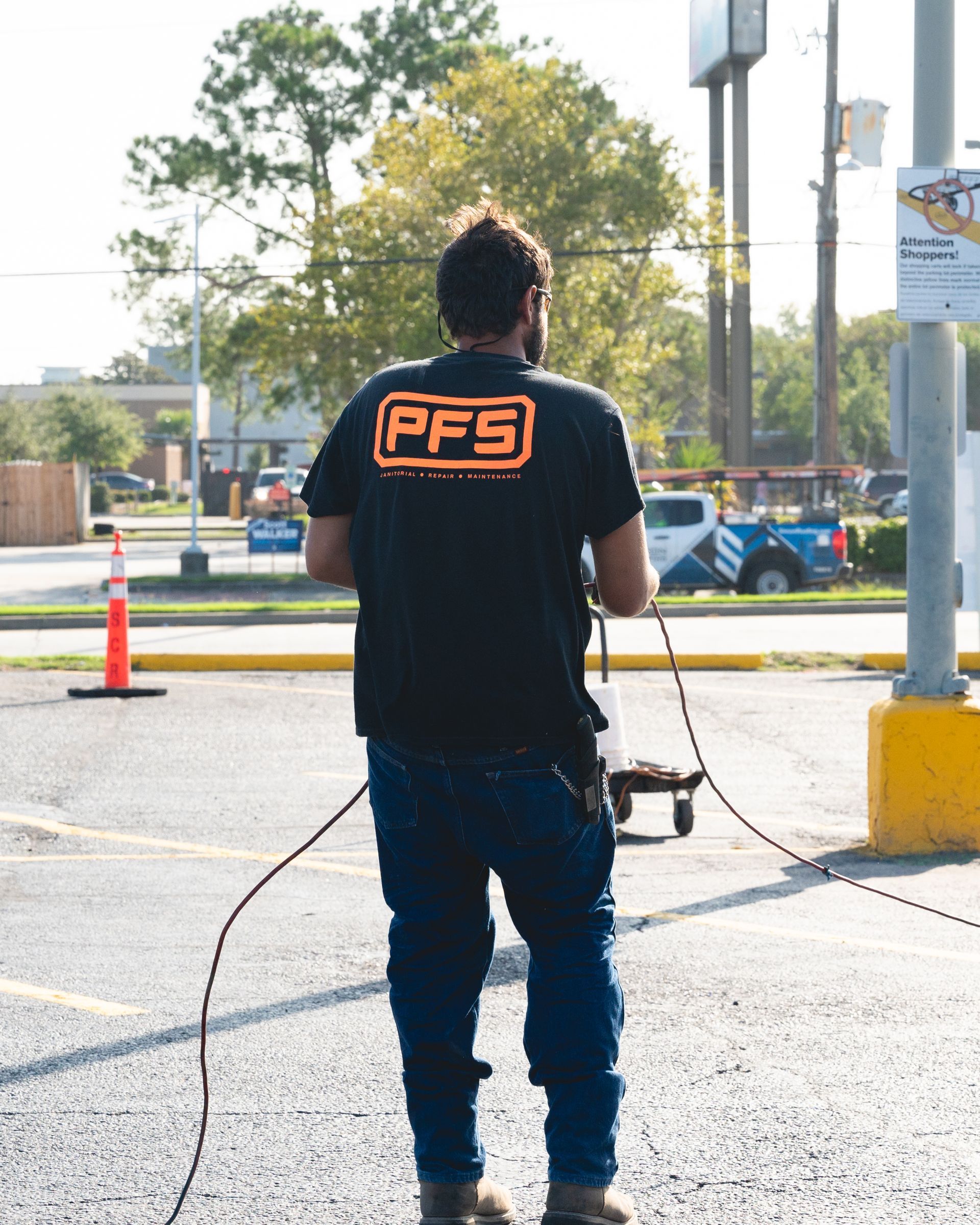 Person in black PFS shirt holding cables in a parking lot near traffic cones and poles