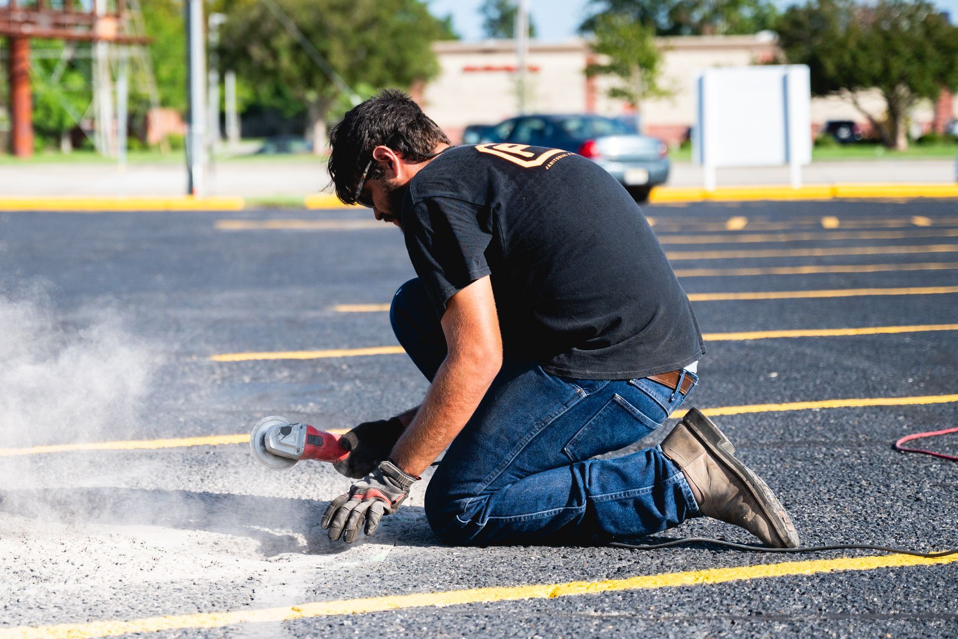 Worker kneeling on asphalt using a power tool, cutting pavement and making dust