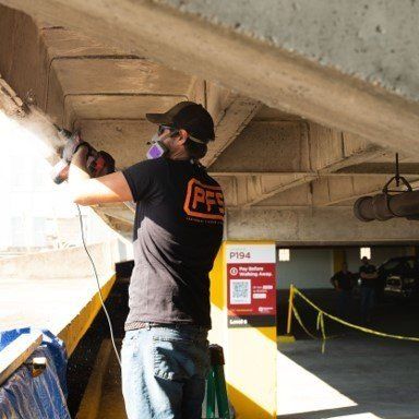 Worker using a power tool to repair concrete under a parking garage ceiling