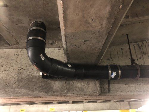 Black insulated ductwork runs along a rough concrete ceiling in an industrial space