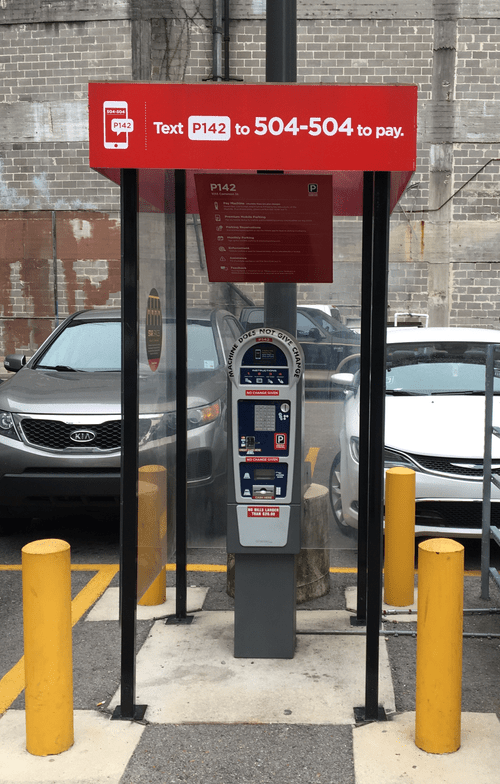 Red emergency call box under red sign, flanked by yellow bollards in a parking lot.