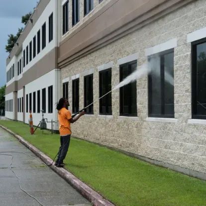 Person pressure-washing the outside of a building with a long spray wand.
