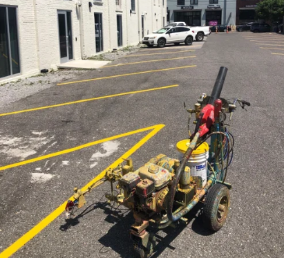 Small homemade wheeled machine with hose and tools parked in a marked lot beside a building