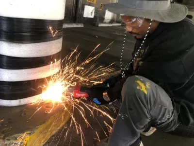 Worker using a grinder on a large black-and-white striped object, sparks flying in a workshop.