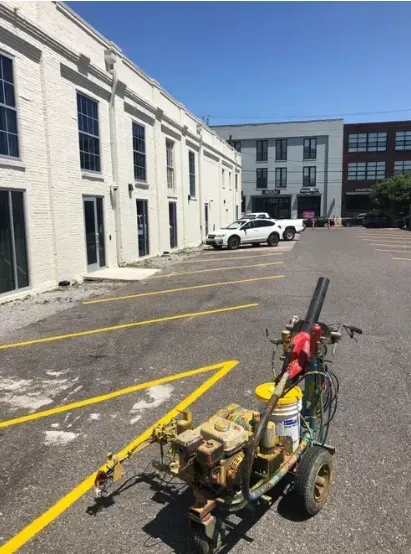 Small motorized cart in a parking lot beside white industrial buildings under a clear blue sky