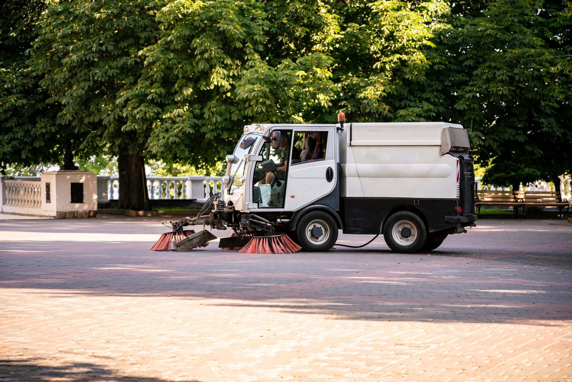 Street sweeper truck cleaning a road in a tree-lined park area