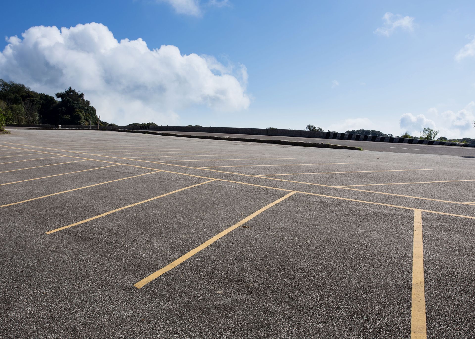 Empty parking lot with yellow lines under a blue sky and clouds