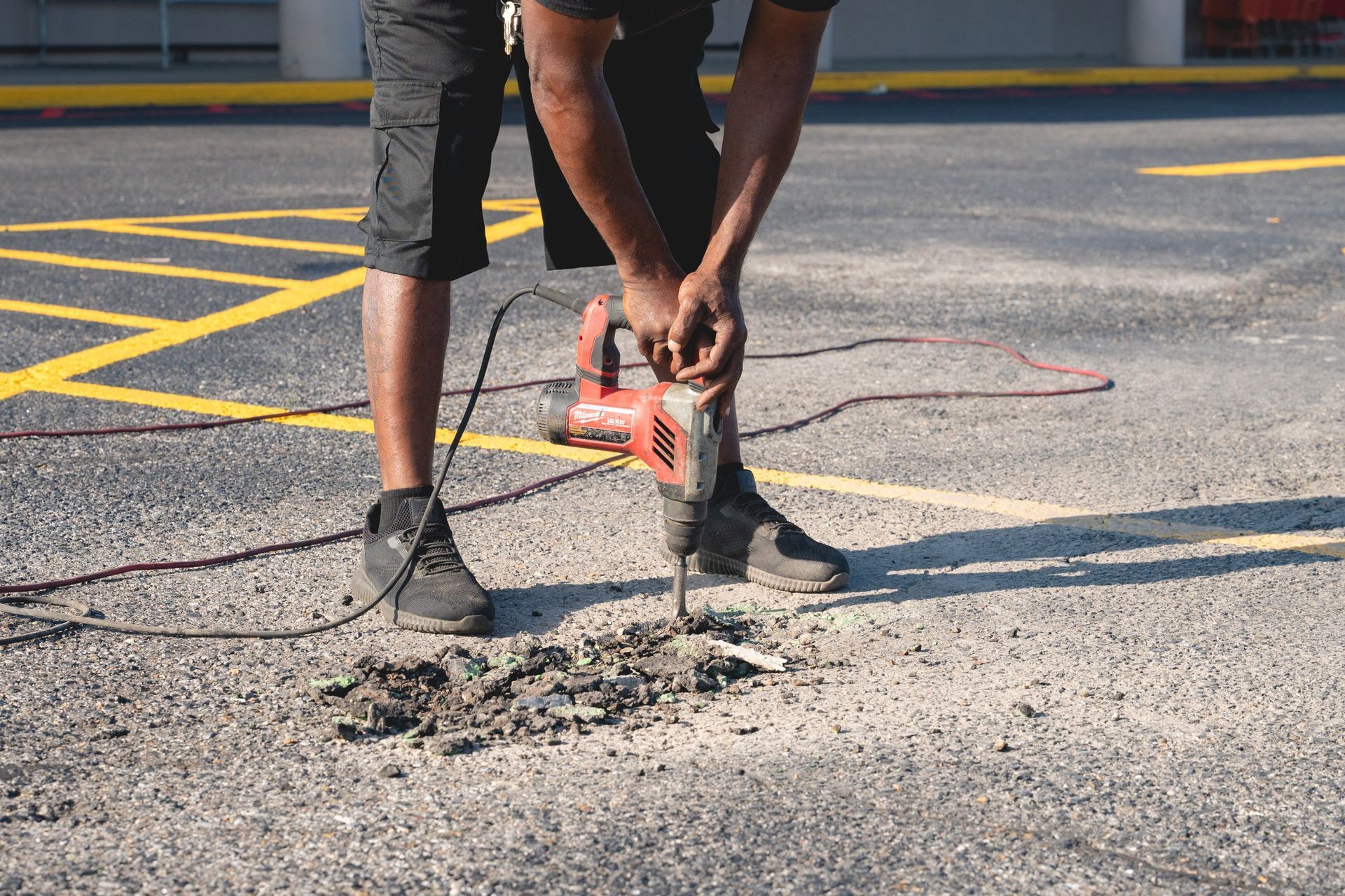 Worker using an orange jackhammer to break concrete on a road surface