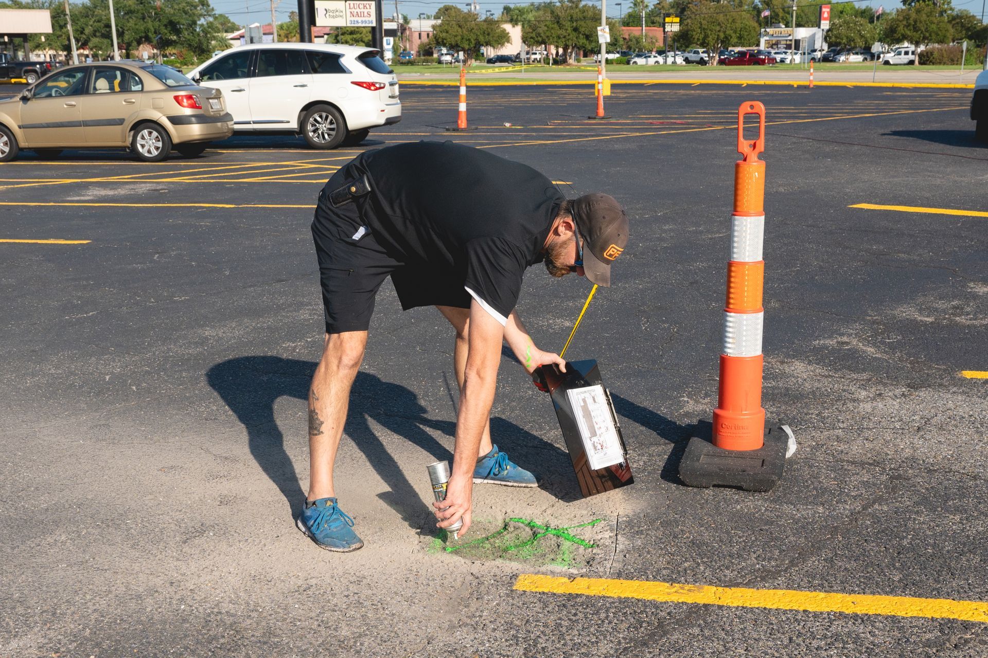 Person bending over to paint a yellow line on asphalt in a parking lot with traffic cones nearby