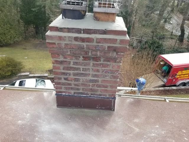 Brick chimney on a rooftop, with a worker in blue nearby and cars visible below.