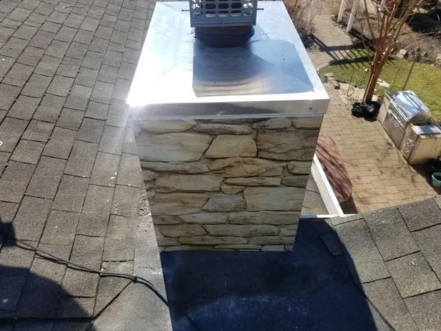 Outdoor chimney with stone veneer and metal cap on a shingled roof