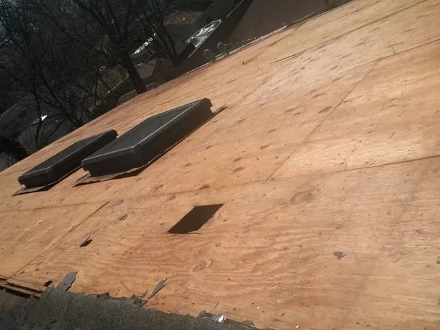 Plywood roof deck with two black vents and a small square opening, viewed at an angle