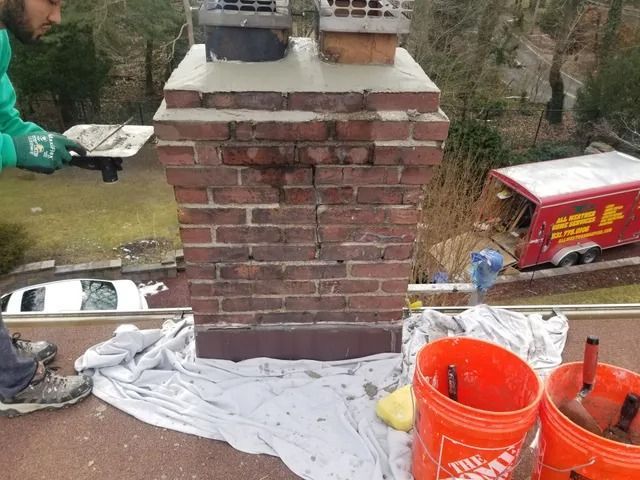 Brick chimney under construction on a rooftop, with orange buckets, tarps, and tools nearby