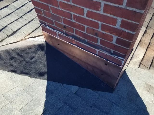 Corner of a brick building with a dark triangular gap at the base on a shingled roof