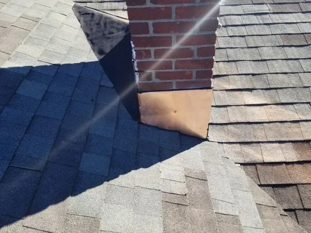 Brick chimney on a shingled roof with sunlight and shadow across gray tiles
