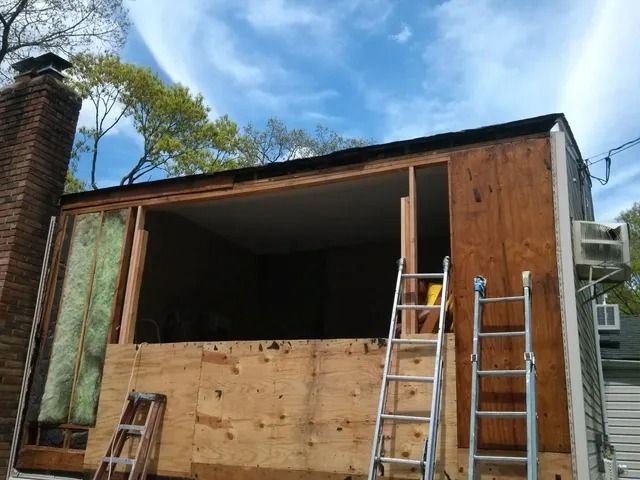 House exterior under renovation with plywood-covered front and two ladders