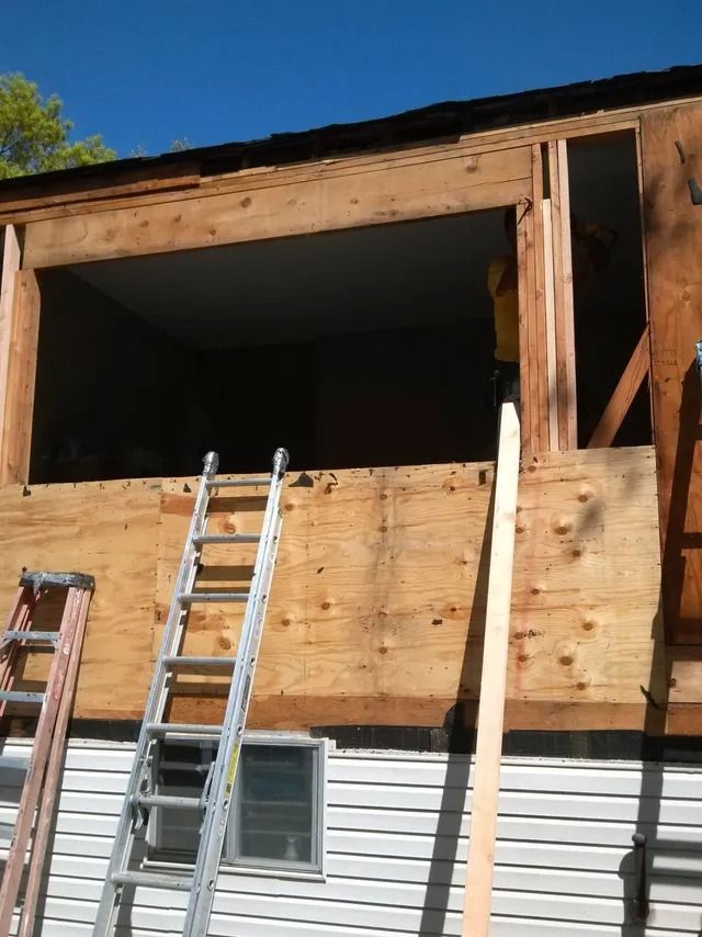 Partially renovated house with exposed wood framing and ladders leaning against the wall