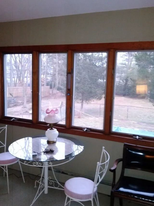 Sunroom with round glass table, white chairs, and large windows overlooking a yard