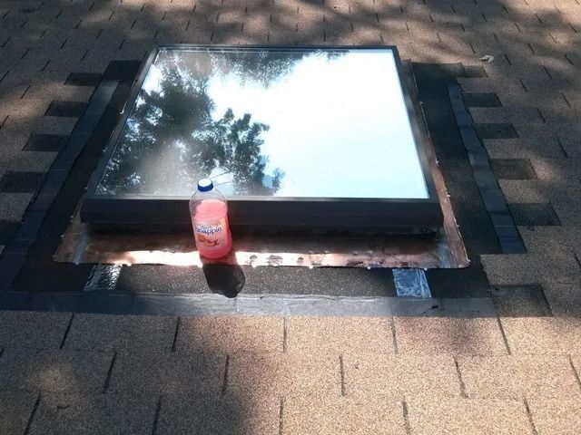 Red bottle on brick pavement beside a reflective glass panel in sunlight.
