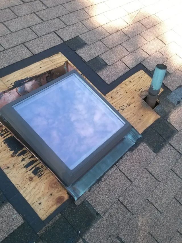 Rooftop skylight with blue glass, surrounded by shingles and wooden flashing panels.