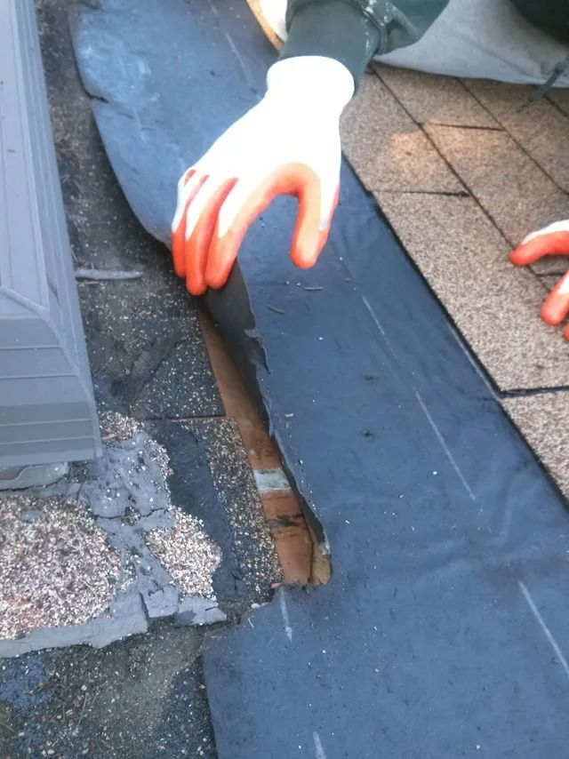 Hands inspecting a damaged roof seam with exposed wood and cracked shingles.