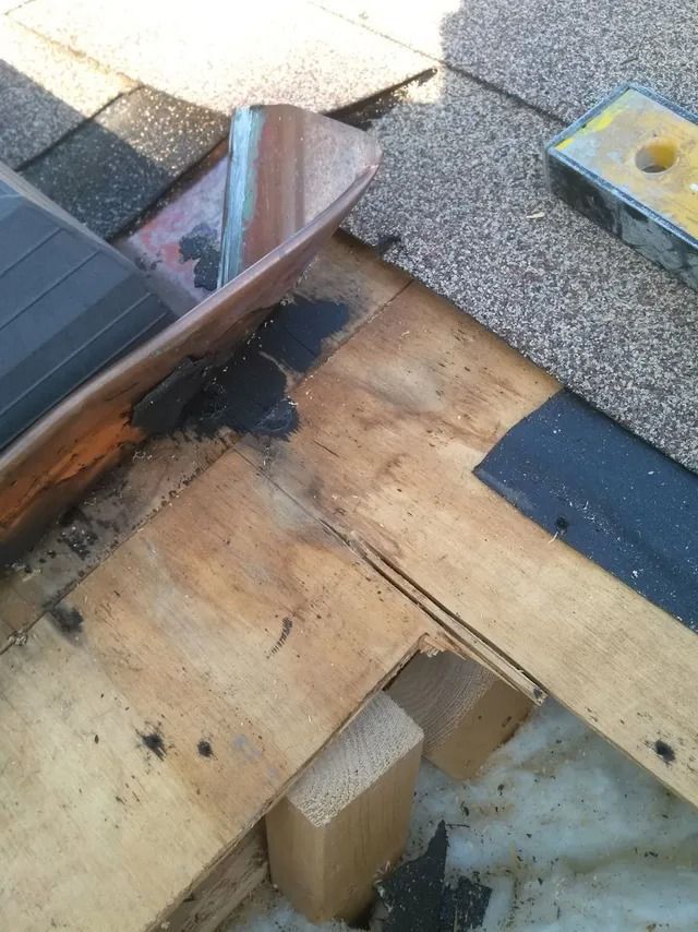 Damaged roof repair with exposed plywood, black tar patch, and shingles at a roof edge
