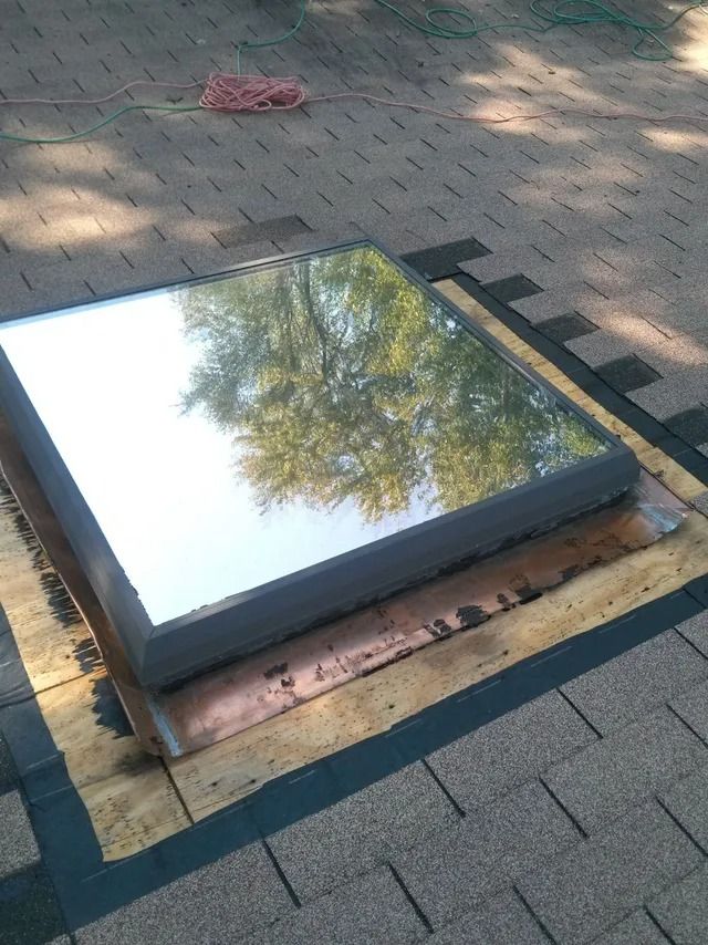 Rectangular reflective panel on a wooden base on a paved sidewalk, reflecting tree branches.