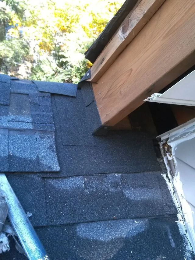 Roof shingles around a dormer with wooden trim, showing a corner and gutter area.