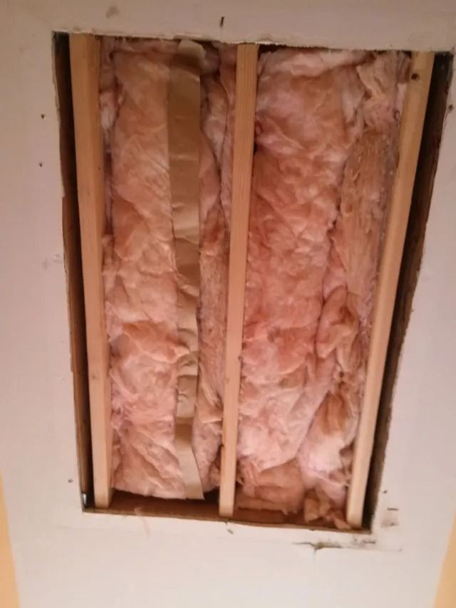 Open wall cavity with pink fiberglass insulation between wooden studs