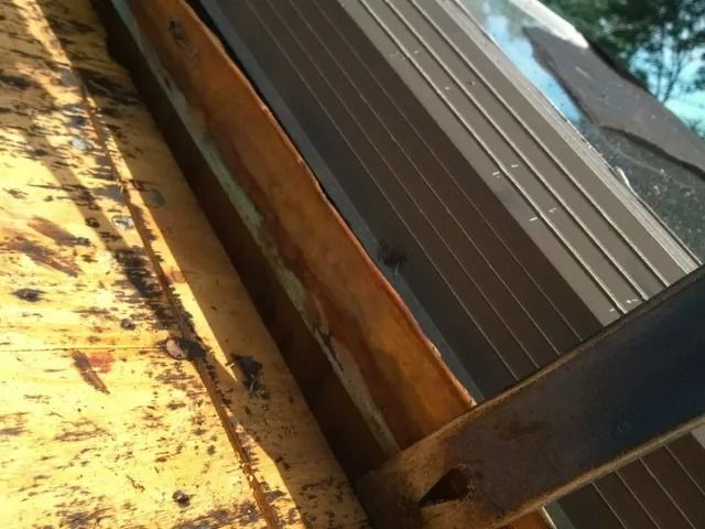 Close-up of a rusted metal roof edge with a brown support beam and a blue roof panel