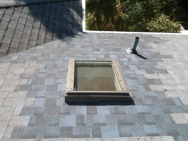 Flat gray shingle roof with a skylight and a small vent pipe.