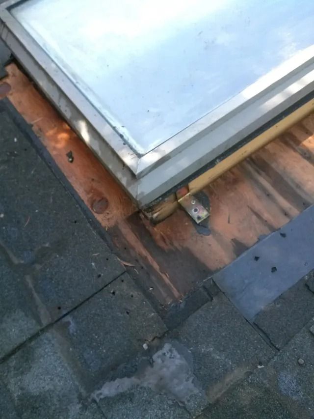 Flat roof corner with a skylight, showing damaged flashing and wet roof shingles.