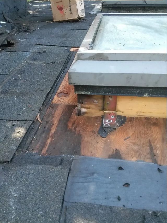 Roof with damaged shingles exposing wood under a rooftop structure and skylight.