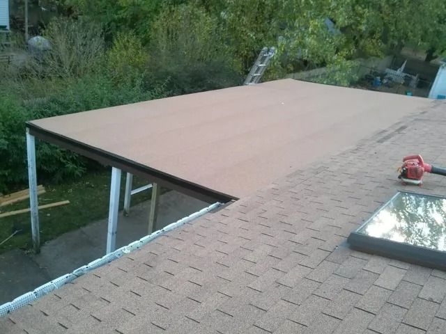 Rooftop under construction with plywood sheets and a red tool near a skylight.