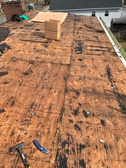 Roof under repair with exposed plywood, tools, and a cardboard box near the ridge