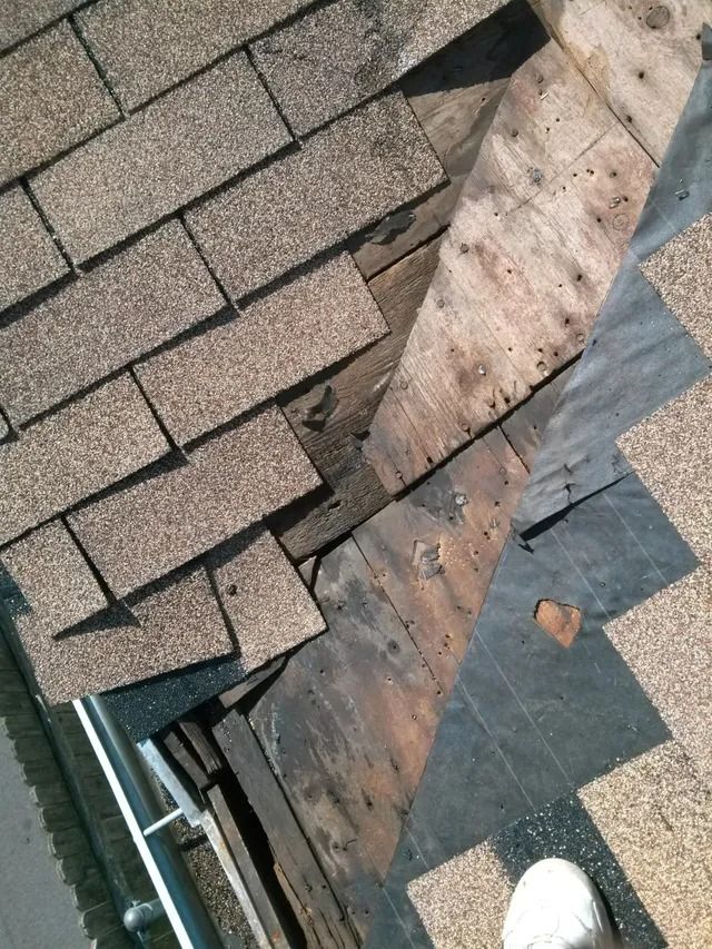 Damaged roof shingles exposing the underlayment near the edge of a roof, with a white boot visible.