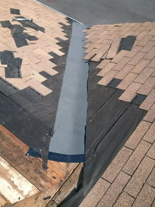 Roof ridge repair with gray flashing between two shingled sections.