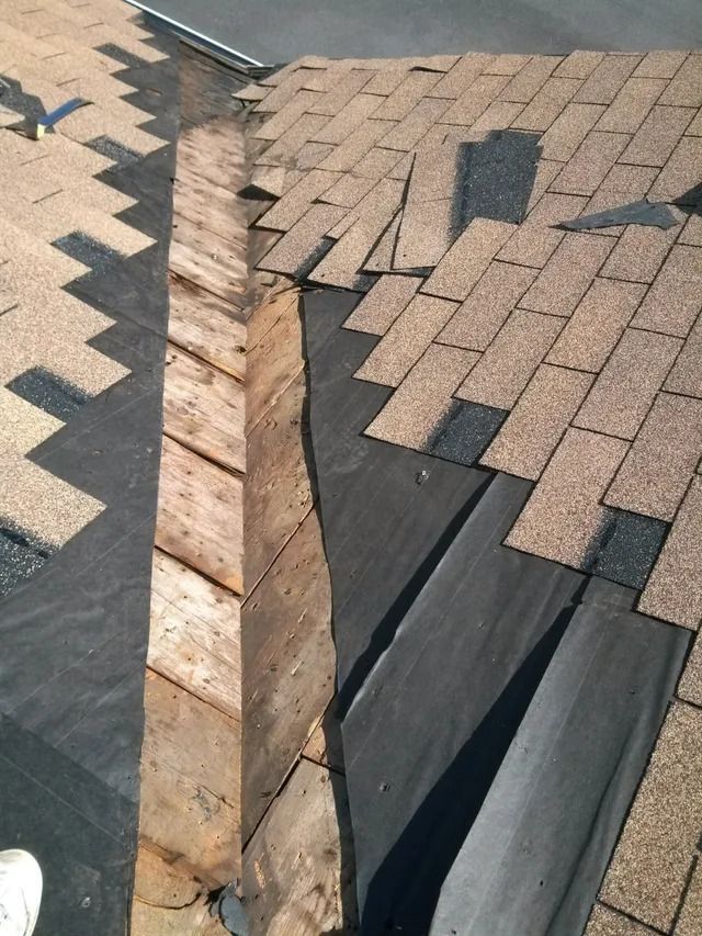 Damaged shingle roof with a gaping tear exposing underlayment and wood decking