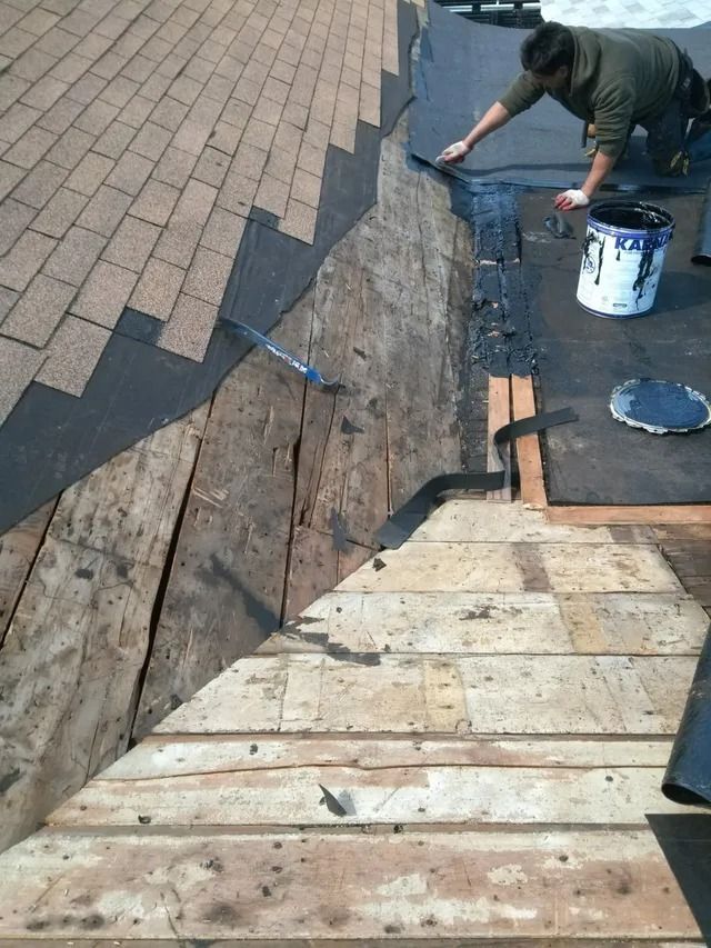 Worker repairing a roof with shingles and a paint bucket nearby