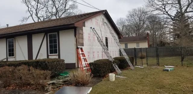Single-story house with white siding and brown trim, ladders leaning against the exterior during repairs
