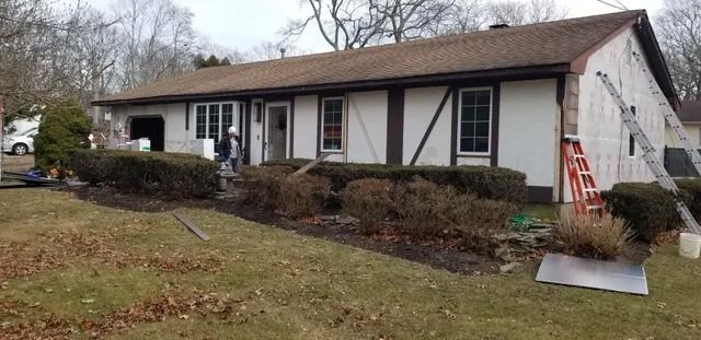 Single-story house with brown roof and white siding on a sloped grassy yard, front steps visible