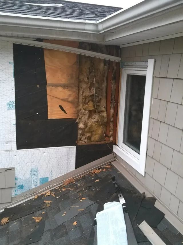 Damaged house wall with exposed insulation and torn roofing near a window and eaves.
