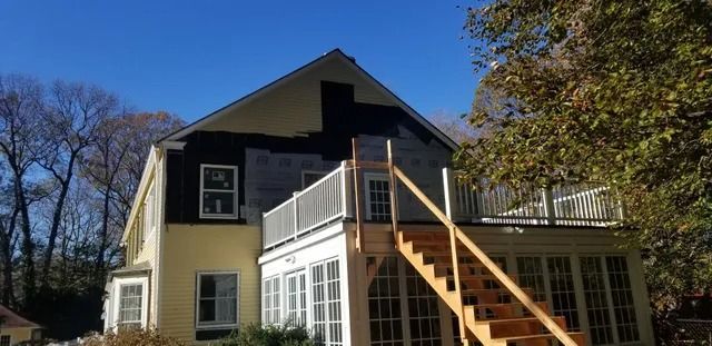 Two-story house with white porch, cream siding, black upper walls, and an exterior wooden staircase