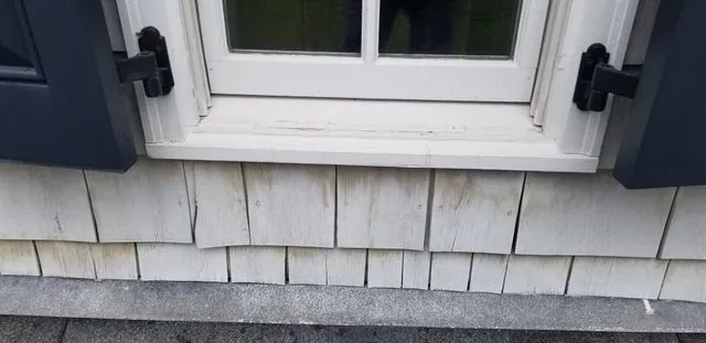 White window with blue shutters above gray shingled siding