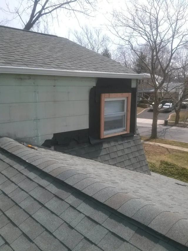 Roof with a dormer window and gray shingles on a house in a residential neighborhood