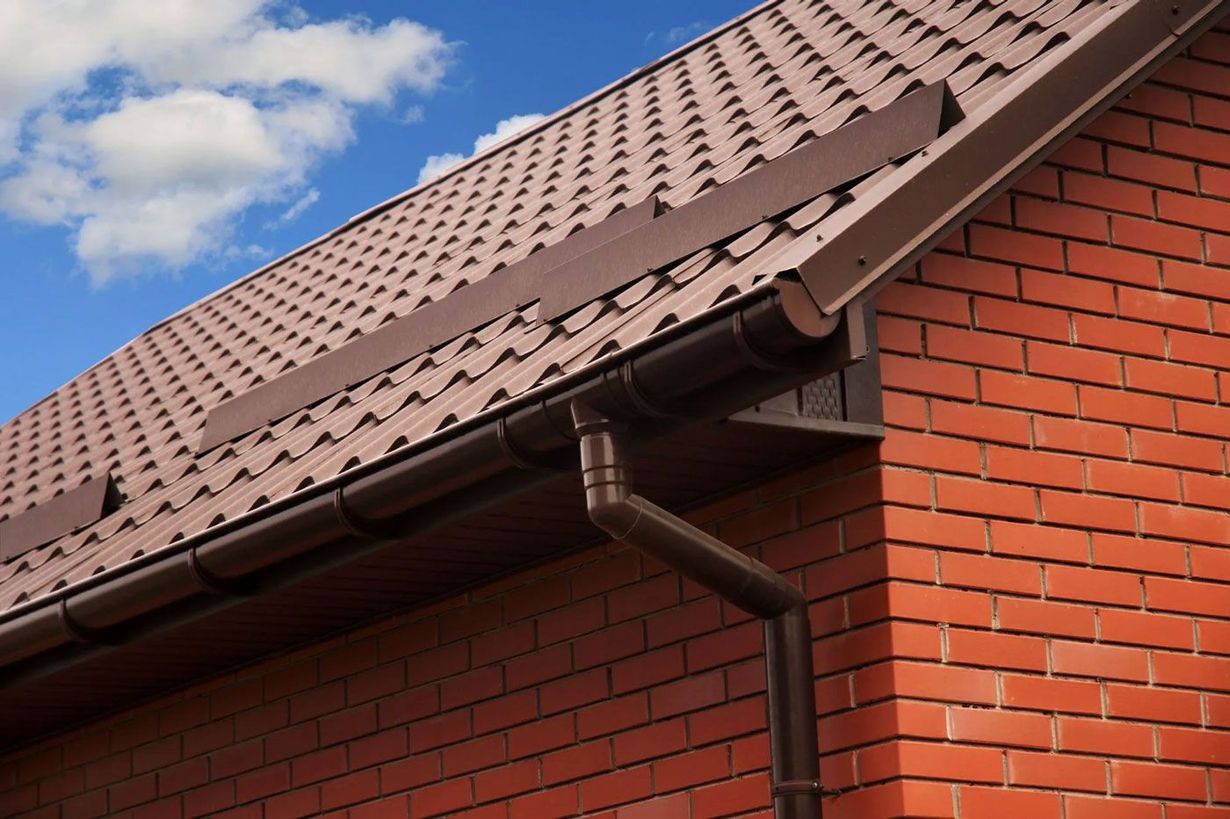 Red brick house with brown tiled roof and rain gutter against a blue sky