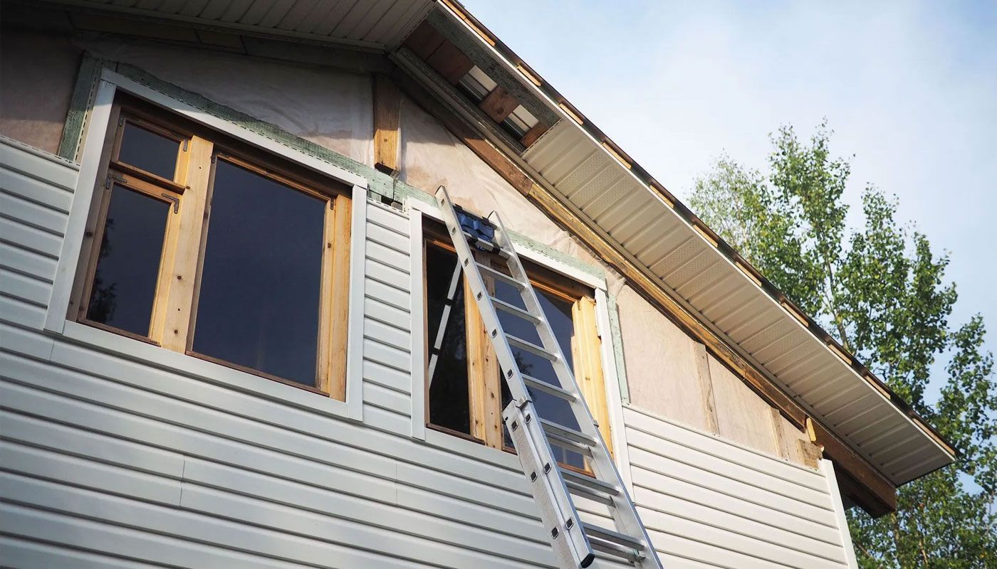 House exterior with open windows and a ladder leaning against the siding under the roof eave